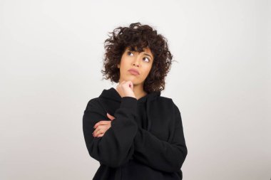 Düşünceli kadın portresi elini çenesinin altında tutuyor, bir şey hatırlamaya çalışıyor ya da ilgi çekici bir şey dinliyor, sıradan giyiniyor, içeride poz veriyor. Gençlik kavramı.