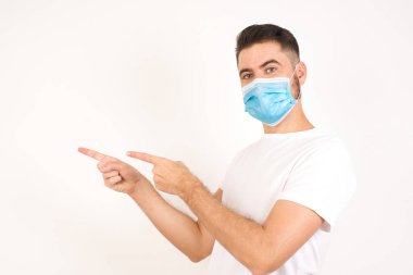 Tıbbi maske takan, ağzı açık, neşeli ve şaşkın bir ifadeye sahip çekici genç adam içeride inanılmaz bir şey gösteriyor. Reklam kavramı.