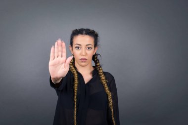 Genç, güzel, İspanyol bir kadın avucunun içi gibi jest yapıyor. Gri arkaplan üzerinde izole edilmiş yüz üzerinde negatif ve ciddi jest içeren uyarı ifadesi. 