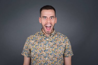 Duygusal genç sarışın adam gündelik kıyafetler giyiyor, yıldönümünü kutlamak için mutlu ve heyecanlı. Mutlu genç adamın morali yerinde Gri duvarda duruyor.