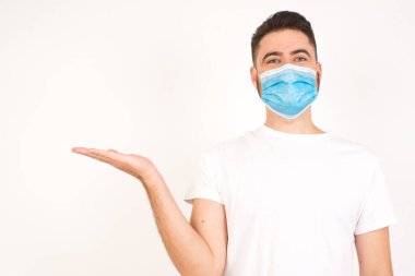 Pozitif memnun erkek der ki: Vay be, ne kadar heyecan verici, hayret verici bir ifade, boş uzayda bir şey gösteriyor, açık elle izole edilmiş gri arkaplan üzerinde. Reklam konsepti. Tıbbi maske takan beyaz bir adam. 
