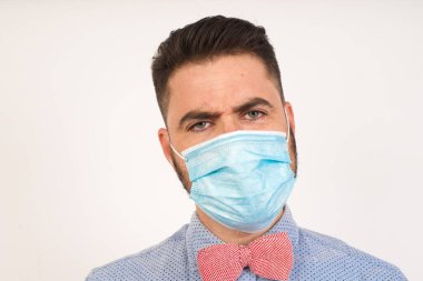 Tıbbi maske takan, düşüncelere dalmış, kaşlarını kaldırmış, dudaklarını kıvırmış, şık kıyafetler giymiş, metnin için gri duvarda duran çekici sarışın adam..