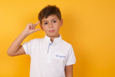 Sarı duvara karşı küçük bir şey gösteren sevimli çocuk.  