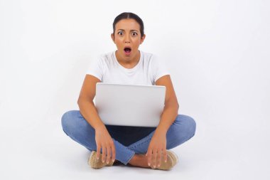 Diz üstü bilgisayarı olan Arap bir kadın ağzı açık ve ağzı açık bir şekilde şaşkın bir şekilde arkadaşının hikayesini dinlerken 