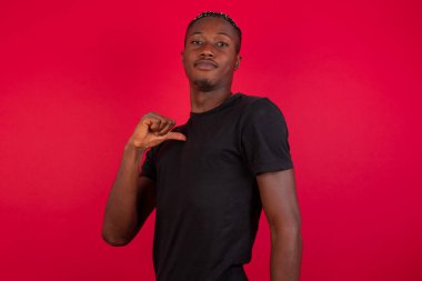 Kırmızı arka planda siyah tişört giyen neşeli, yakışıklı Afro-Amerikalı adamın yakın çekimi neşeli, memnun ve kendinden emin görünüyor..