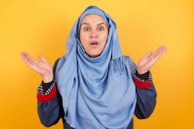 Sürpriz konsept. Şaşırmış orta yaşlı, tesettürlü Müslüman bir kadının portresi. İnançsızlığa kapılmış, ağzı açık ve elleri yüzüne yakın bir şekilde bakıyor. 