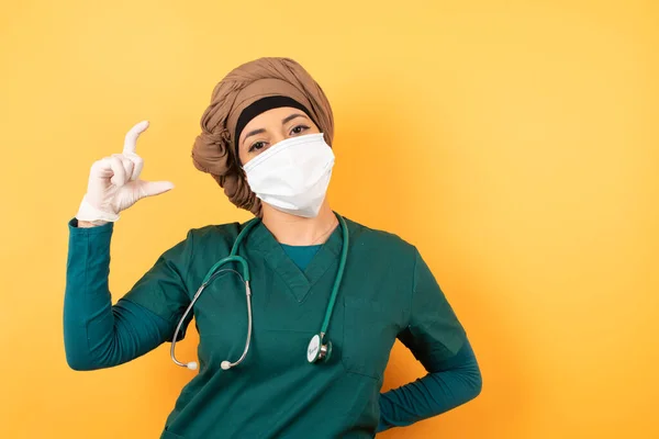 緑色の医療制服の若い美しいイスラム教徒の医師女性は 小さなサイズを示す手でジェスチャーし シンボルを測定します カメラを見ている笑顔 測定コンセプト — ストック写真