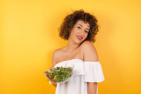 Shy girl smiling looking to the camera. Caucasian charming girl sanding against gray studio background feeling shy.