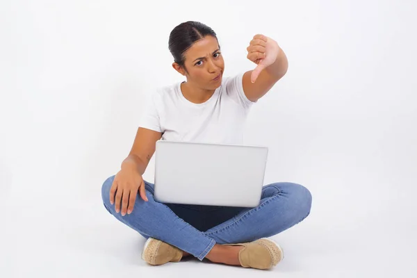 不満の女性は不承認の印を示し 親指を保ち 不満で不満を表し 白いシャツを身に着け 灰色の背景に隔離された顔を凍らせます ボディランゲージコンセプト ラップトップコンピュータを使用して若い美しいアラブの女性 — ストック写真