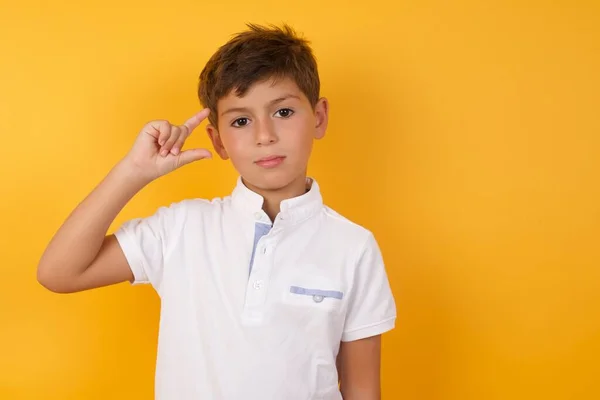 Χαριτωμένο Αγόρι Δείχνει Κάτι Μικρό Ενάντια Στον Κίτρινο Τοίχο — Φωτογραφία Αρχείου
