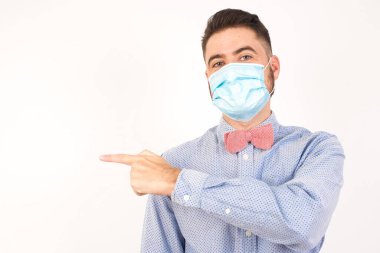 Şuraya bakın! Yakışıklı, sarışın, beyaz, tıbbi maske takan, gri arka planda dururken sana gülümseyen adam..