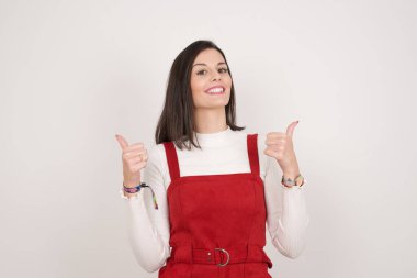 Gri arka planda izole edilmiş, olumlu içerik ve mutluluk duygularıyla baş parmaklarını gösteren iyimser genç bayana yakın çekim. Ortak alan, kalite ve tavsiye ile tatmin kavramı.