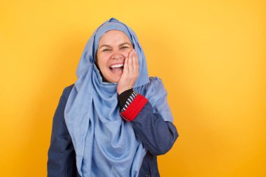 Şaşırmış, orta yaşlı, tesettürlü Müslüman bir kadın şaşkınlık içinde, ağzı açık, eli yüzü yere yakın bir şekilde şaşırmış görünüyor.. 