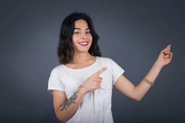 Olumlu ifadeli güzel esmer kadın, sıradan giyinmiş, promosyon metnin ya da ilanın için boş fotokopi alanında ön parmağınla işaret ediyor. Sevimli kadın evde tek başına poz veriyor.