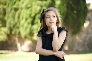 Siyah elbiseli, hoş bir yüzü olan, sıradan kıyafetler giyen, yan bakan, elini çenesinin altında tutan, hoş bir şeyler düşünen, poz veren tatlı bir kız. 