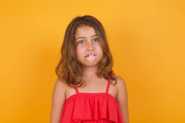 Sarı arka planda poz veren kırmızı elbiseli tatlı küçük kız. 
