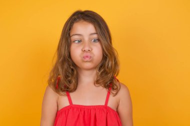 Sarı arka planda poz veren kırmızı elbiseli tatlı küçük kız. 