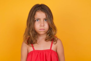 Sarı arka planda poz veren kırmızı elbiseli tatlı küçük kız. 