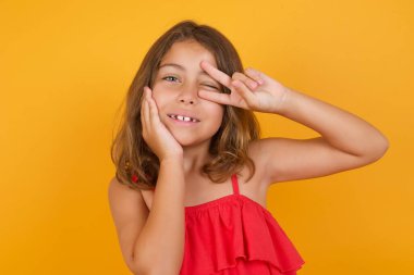 Sarı arka planda poz veren kırmızı elbiseli tatlı küçük kız. 