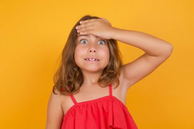 Kırmızı elbise giyen küçük tatlı kızın sarı arka planda kafası karışmış. 