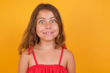 Sarı arka planda poz veren kırmızı elbiseli tatlı küçük kız. 