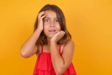 Kırmızı elbise giyen küçük güzel kızın sarı arka planda kafası karışmış. 