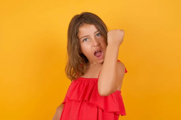 Sarı Arka Planda Yumruğunu Gösteren Kırmızı Elbiseli Sevimli Küçük Kız — Stok fotoğraf