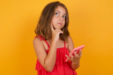Sarı arka planda akıllı telefonu olan kırmızı elbiseli güzel bir kız. 