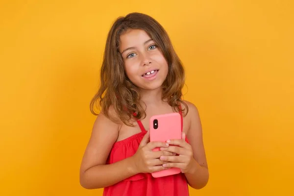 黄色の背景にスマートフォンを保持する赤いドレスを身に着けている美しい少女 — ストック写真