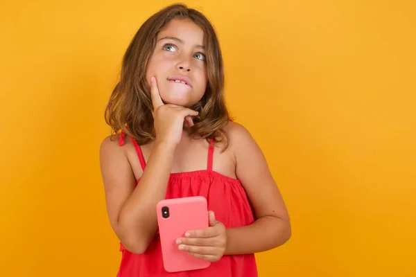 Beautiful Little Girl Wearing Red Dress Smartphone Thinking Yellow Background — Stock Photo, Image