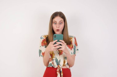 Gri arka planda izole edilmiş güzel bir bayanın yatay görüntüsü, böcek gözlü, modern akıllı telefonu elinde tutan, arkadaşından beklenmedik bir mesaj alan,.