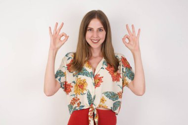 Çekici bir kadının iki eliyle de tamam işareti göstermesi sevindirici bir ifade. Güzel bir kadının fotoğrafı çekici bir görünüme sahip, iyimser olmak. Gri duvara yaslanarak.