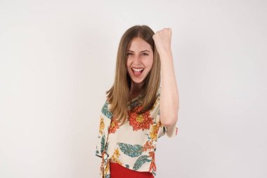 Sevinçten havalara uçmuş, heyecanlı, mutlu, güzel haberler almaktan memnun, mutluluktan hareketler yapan, yumruğunu sıkan ve kazanan bir jest yapan sarışın kadın. Tepki konsepti.