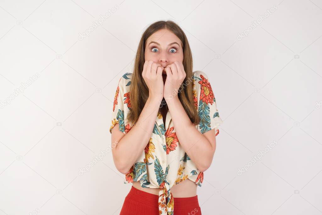 Anxiety - a conceptual image of a beautiful young caucasian woman covering her mouth with her hands and standing outdoors. Scared from something or someone bitting nails.