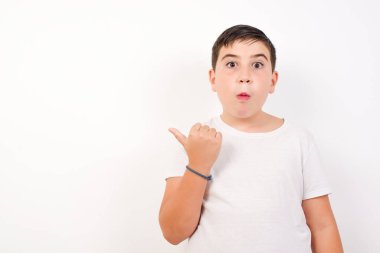 Genç ve neşeli çocuğun başparmağıyla işaret ettiği yatay çekim beyaz arka planda izole edilmiş boş bir duvara işaret ediyor..