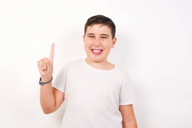 Gri beyazın karşısında duran beyaz çocuk bir numaralı parmağını gösterip gülümserken kendinden emin ve mutlu..