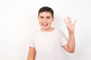 Beyaz duvarın önünde duran genç çocuk beş numarayı gösterip işaret ederken kendinden emin ve mutlu gülümsüyor..