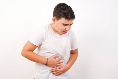 Beyaz arka plan üzerine gündelik kıyafetler giyen genç yakışıklı çocuk güçlü bir karın ağrısı çekiyor..