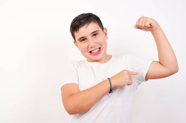Sarışın çocuğun belden yukarı pozu kaslarını göstermek için elini kaldırır, zaferden emin olur, güçlü ve bağımsız görünür, kameraya olumlu gülümser, beyaz arka planda durur. Spor konsepti. 