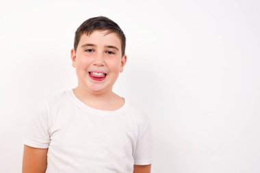 Gülümseyen ve dil gösteren mutlu ve komik yüzlü güzel beyaz çocuk. Günlük giysiler giyip beyaz stüdyo geçmişine karşı durmak..