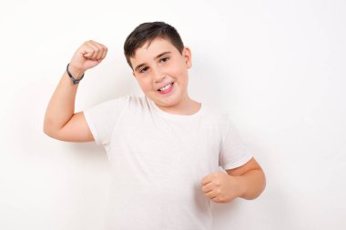 Çekici beyaz çocuk zaferi kutluyor yumruklarıyla gökyüzünü yumrukluyor ve beyaz stüdyo arka planında ışıltılı bir gülümseme ile fotokopi çekiyor.