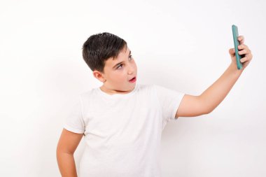 Arkadaşlarına ve takipçilerine göndermek için selfie çeken yakışıklı beyaz bir çocuğun portresi ya da beyaz arka planda izole bir şekilde sosyal medyasına yüklemek..