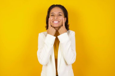 Güçlü, sağlıklı, beyaz dişlere sahip olma kavramı. Arka planda izole edilmiş, kusursuz beyaz dişlerini gösteren, ışıl ışıl gülümseyen, gündelik kıyafetler giyen genç beyaz kadın portresi..