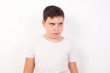Şaşırmış genç çocuğun fotoğrafı dudaklarını kıvırır ve endişeli bakar, önünde korkunç bir şey görür, beyaz arka planda izole edilmiş, kot pantolon giymiş..