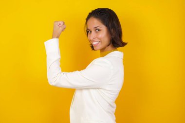 Sarı arka planda izole edilmiş güzel beyaz kadın portresi egzersiz yaptıktan sonra kaslarını gösteriyor. Sağlık ve güç kavramı