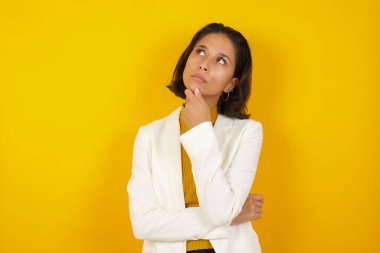 Düşünceli gülümseyen kızın portresi elini çenesinin altında tutuyor, yan bakıyor, ilgi çekici bir şey düşünüyor ya da merak ediyor, sıradan giyiniyor, stüdyo duvarına karşı poz veriyor. Karar alma kavramı.