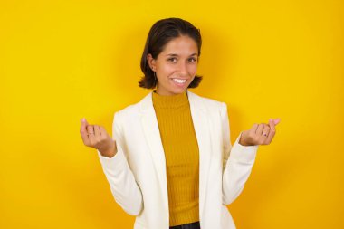 Sarı arka planda sıradan giysiler içinde duran güzel iş kadınının şık bir stüdyo portresi. Güzel bir el kol hareketi. 
