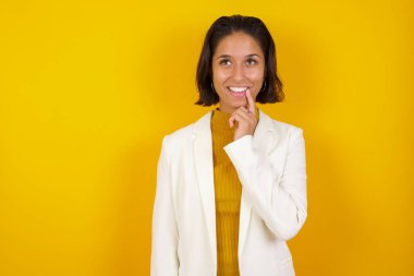 Hayalperest bir kadın, düşünceli bir ifadeyle, kameraya bakıyor, yüzüne yakın duruyor, parmağını ısırıyor, hoş bir şey düşünüyor, duvara karşı poz veriyor..