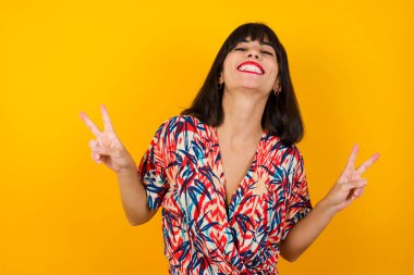 Neşeli kadın vuruşu iki eliyle barış ya da zafer işareti yapar, günlük kıyafetler giyer, serin hisseder dişli bir gülümsemesi vardır. İnsanlar ve vücut dili.