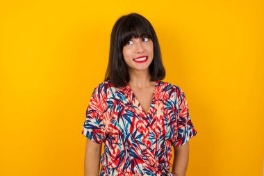 Genç, güzel, beyaz, günlük kıyafetler giyen bir kadın sarı arka plana bakıyor. 